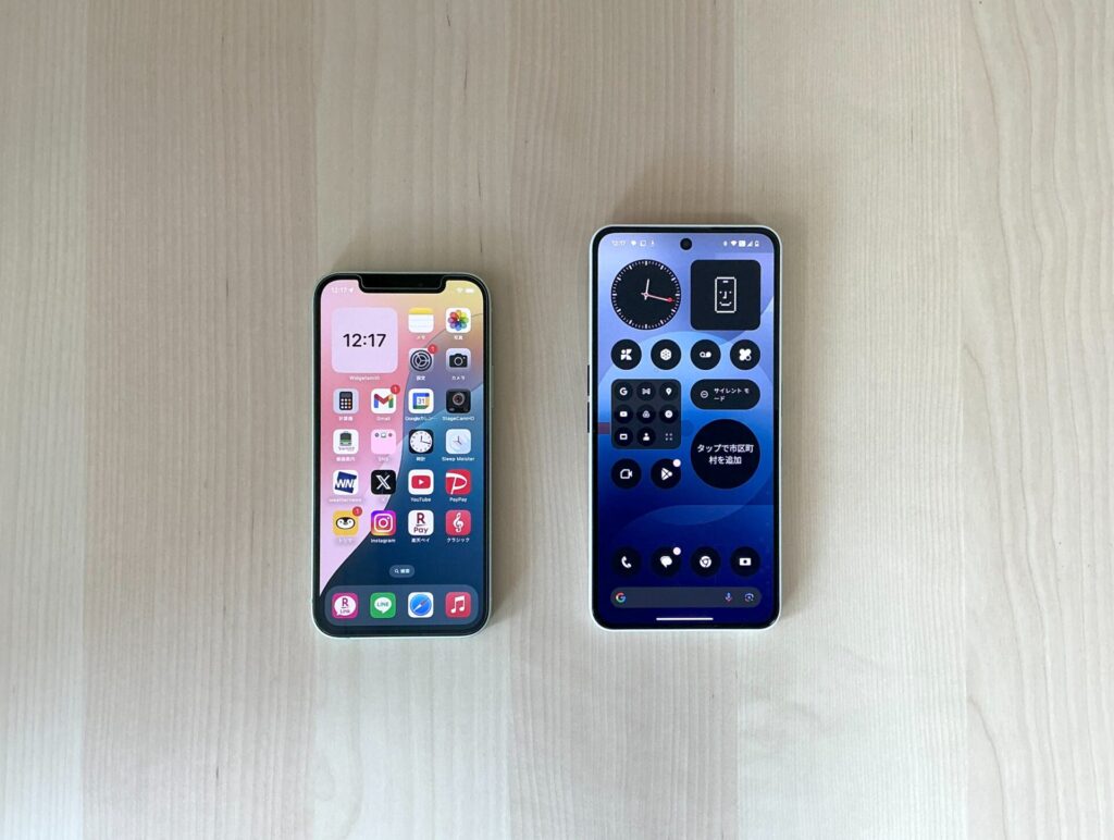 iPhone12とNothingのPhone(3a)の画面が並べて置いてある。Phone(3a)はアプリアイコンがモノクロになっている。